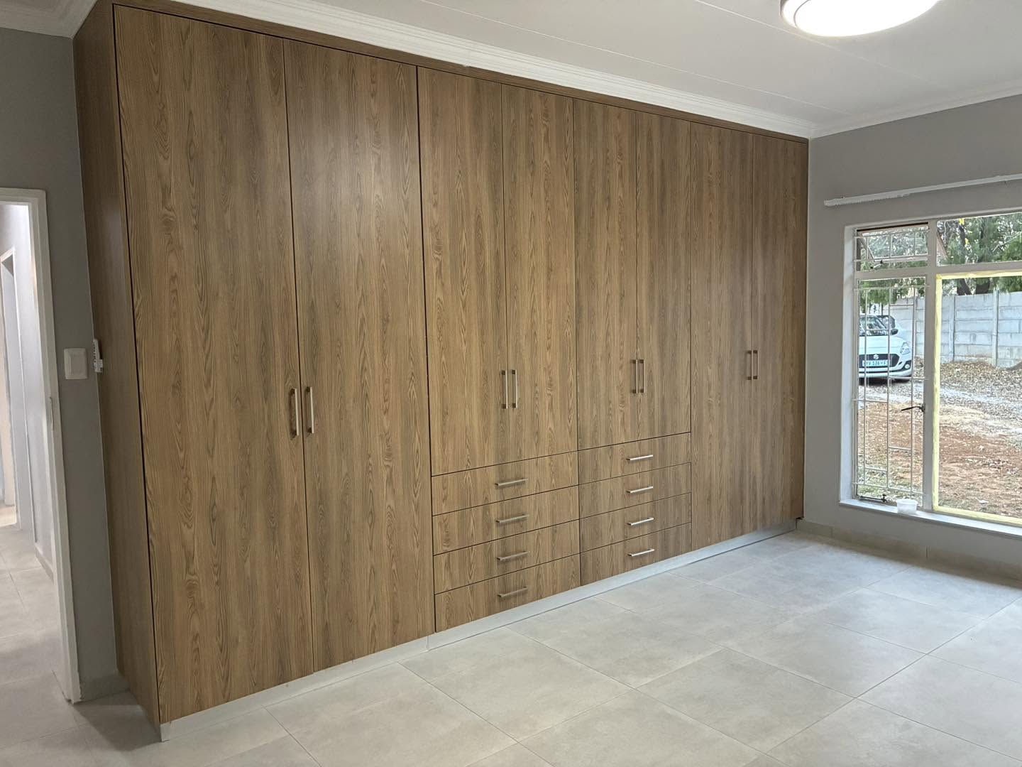 Wood-grain wall-to-wall bedroom cupboards with drawer bank